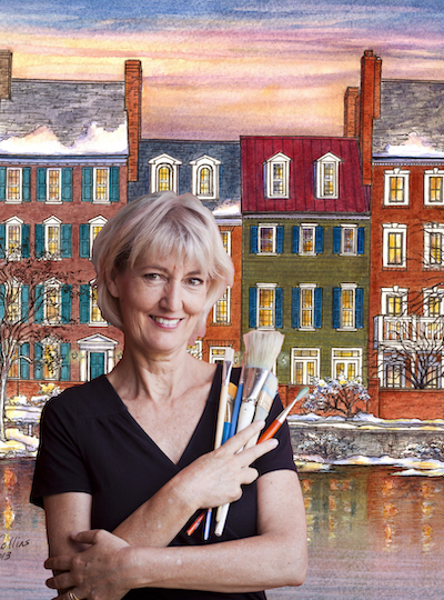 artist Leisa Collins standing in front of painting of townhomes holding art brushes