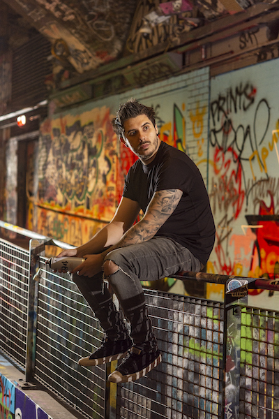 artist Rich Simmons seated on metal rail with graffiti art behind | on Art Biz Success