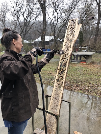 artist Christine Aaron standing burning holes into wood slice | on Art Biz Success