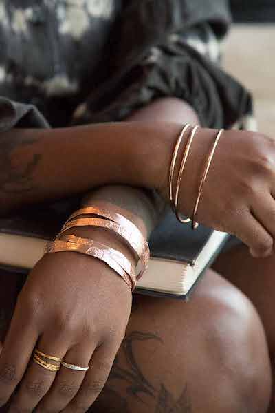 arms with gold bangles crossed over a book resting on a knee | on Art Biz Success