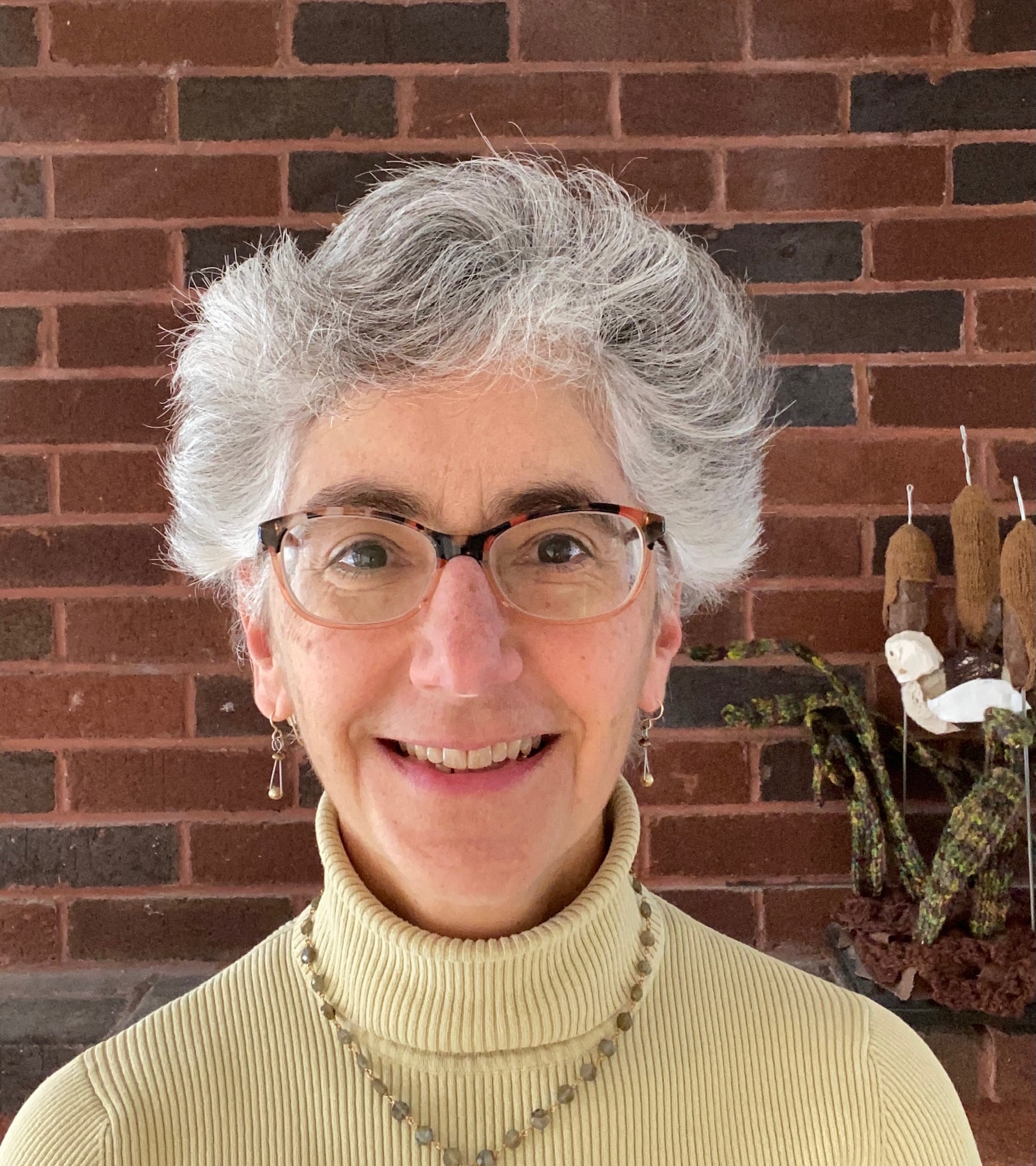 artist Eve Jacobs-Carnahan with short gray hair black rimmed glasses yellow turtleneck and dangly jewelry