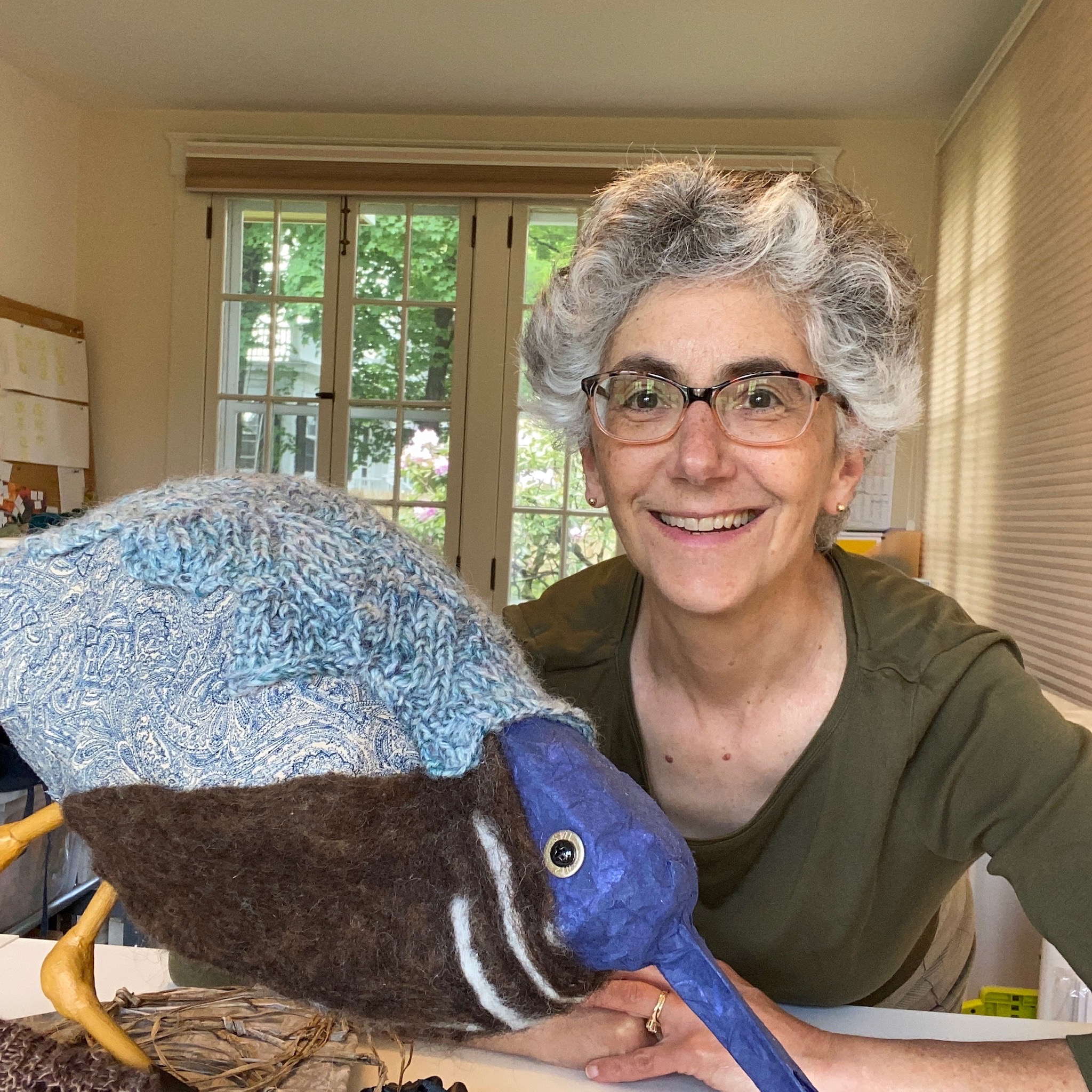 artist Eve Jacobs Carnahan with short gray hair smiling with knit bird sculpture | on Art Biz Success