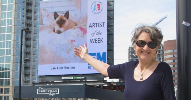 artist Jan Alice pointing at a billboard featuring her