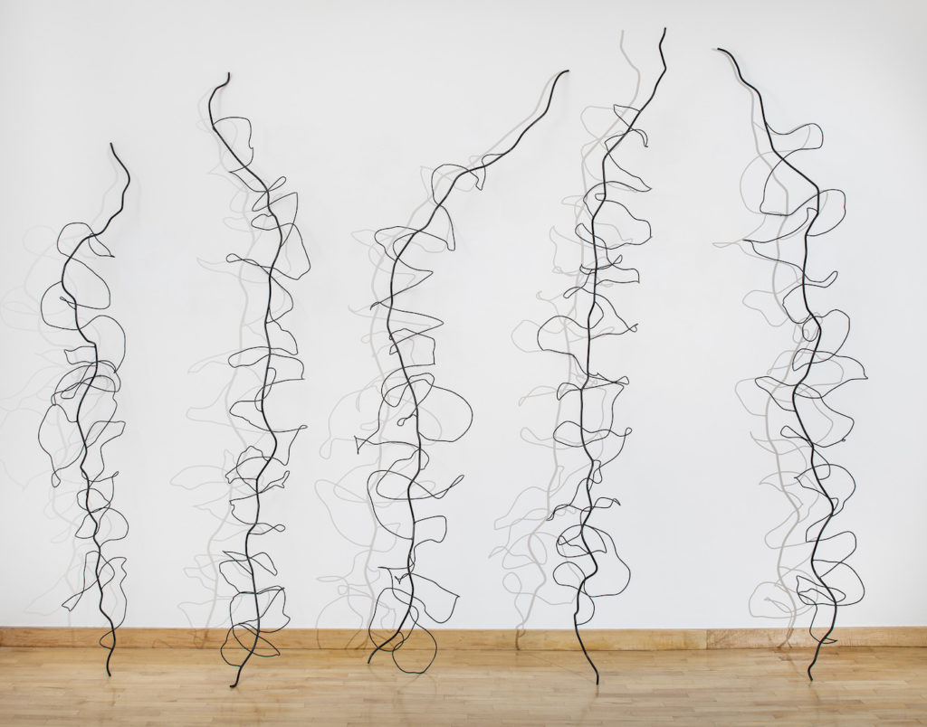 Steel wire sculptures of vine outlines on a light wood floor with white wall behind | on Art Biz success