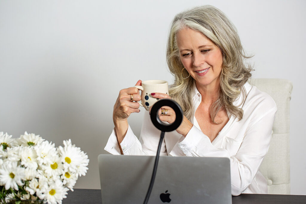 Alyson Stanfield looking at her laptop with daisies and holding a coffee cup by artist Nicole Copel.