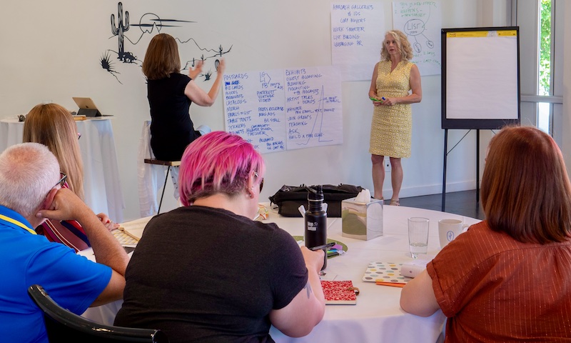 Alyson Stanfield teaching a live workshop in Scottsdale in 2019. She's strategizing with an artist and recording notes.