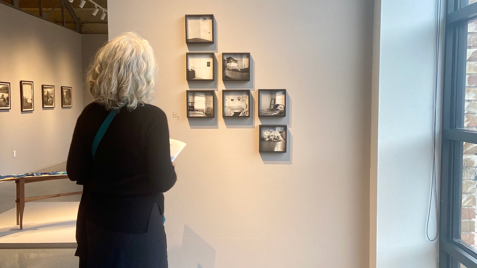 Woman in black outfit looking at black-and-white images on a gallery wall.