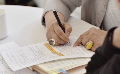 Woman's hands with large rings writing on a worksheet.