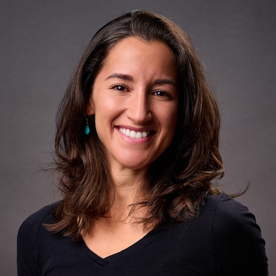Photo of Jenny McCarty, a woman with shoulder-length dark hair and wearing a black v-neck shirt.